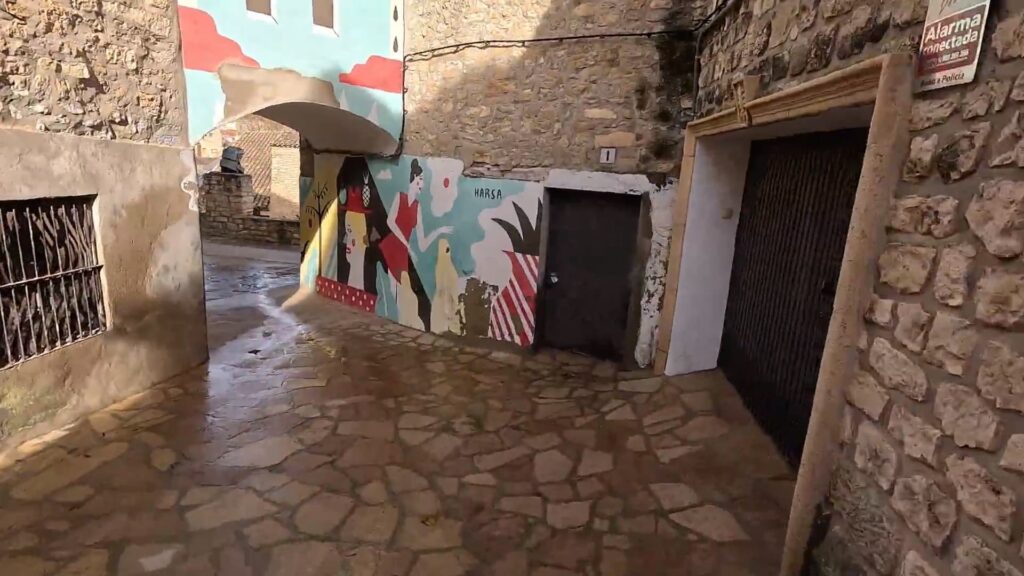 Callejón empedrado de Fuendetodos con un mural artístico colorido pintado sobre una pared de piedra.