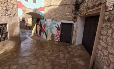 Callejón empedrado de Fuendetodos con un mural artístico colorido pintado sobre una pared de piedra.