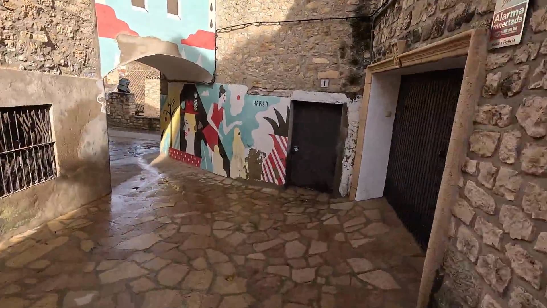 Callejón empedrado de Fuendetodos con un mural artístico colorido pintado sobre una pared de piedra.