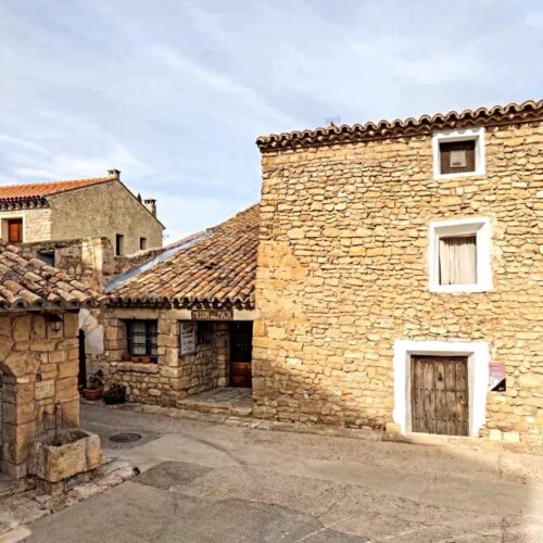 Casas tradicionales de piedra con tejados de arcilla se alzan en una plaza rústica de Fuendetodos.